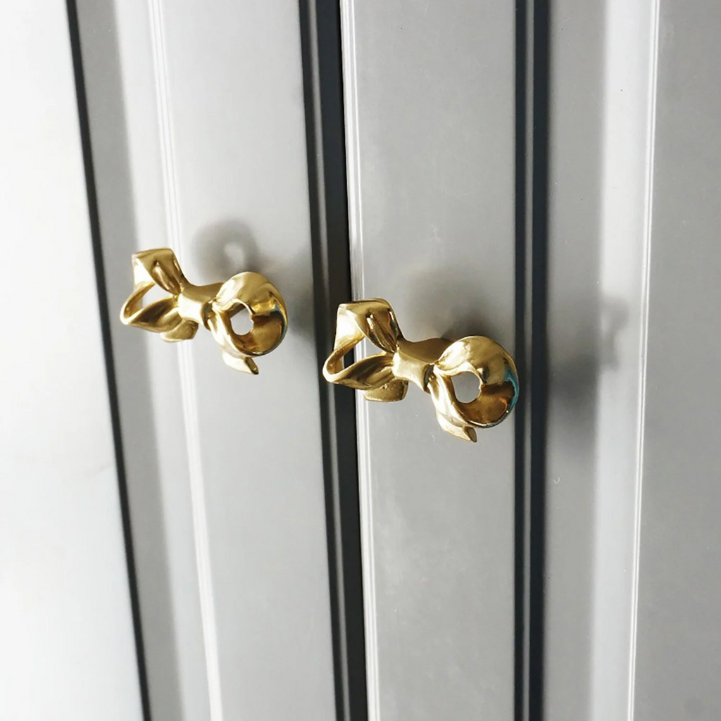 Polished brass bow cabinet knob by Brass Essence, showing a shiny, elegant curved handle for furniture decor.