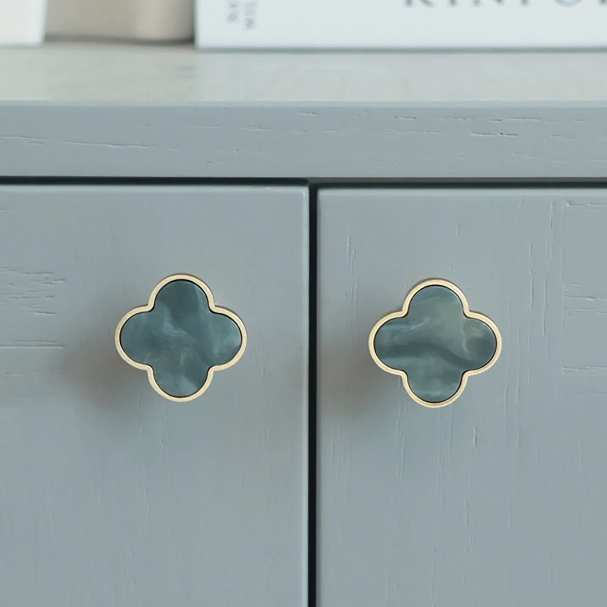 Brass essence Clover Brass Cabinet Knob from collection A-0006, showing a polished brass finish and rounded design on a wood cabinet door.